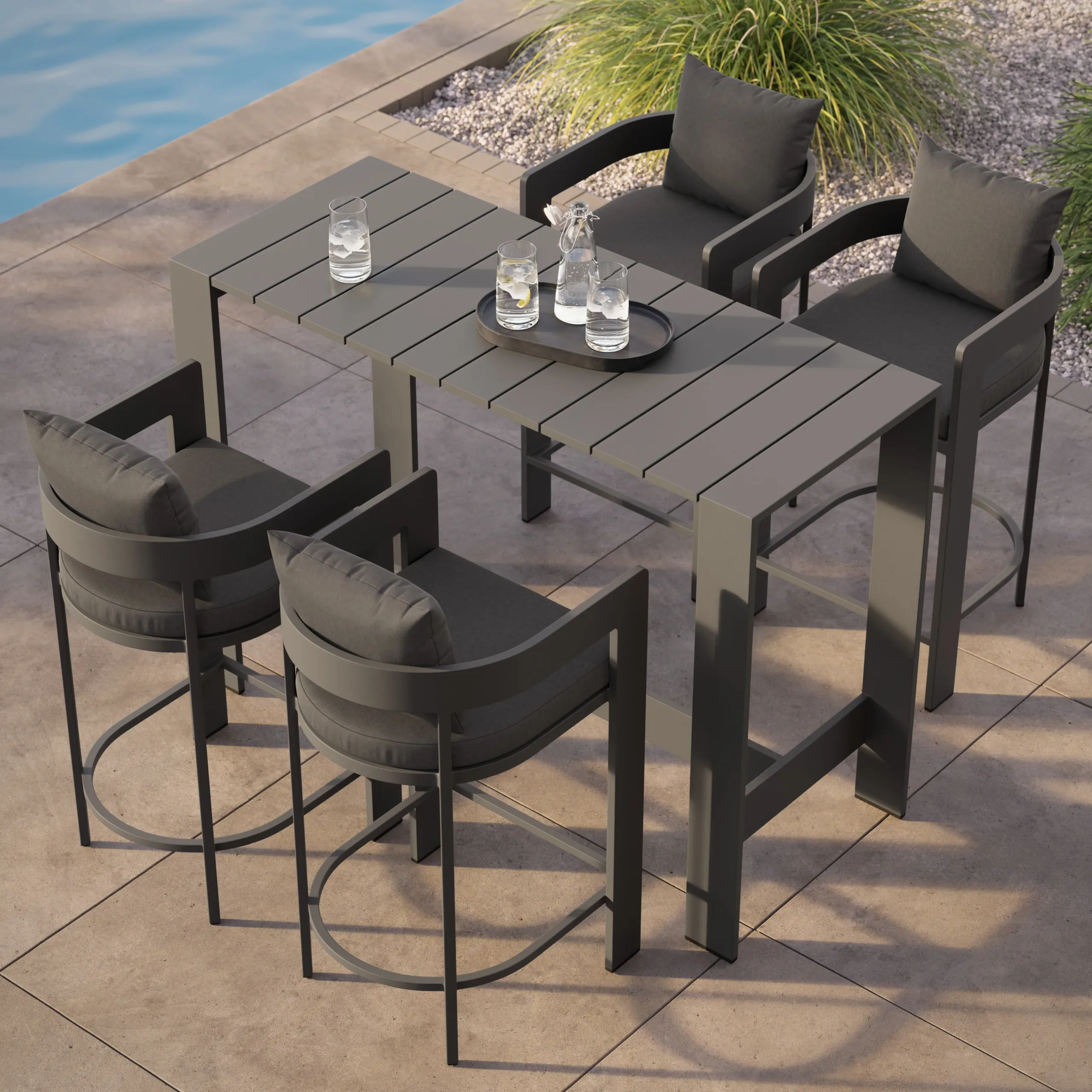 Dark gray outdoor high dining table with four cushioned bar chairs on a patio next to a pool, tray with water glasses on table.