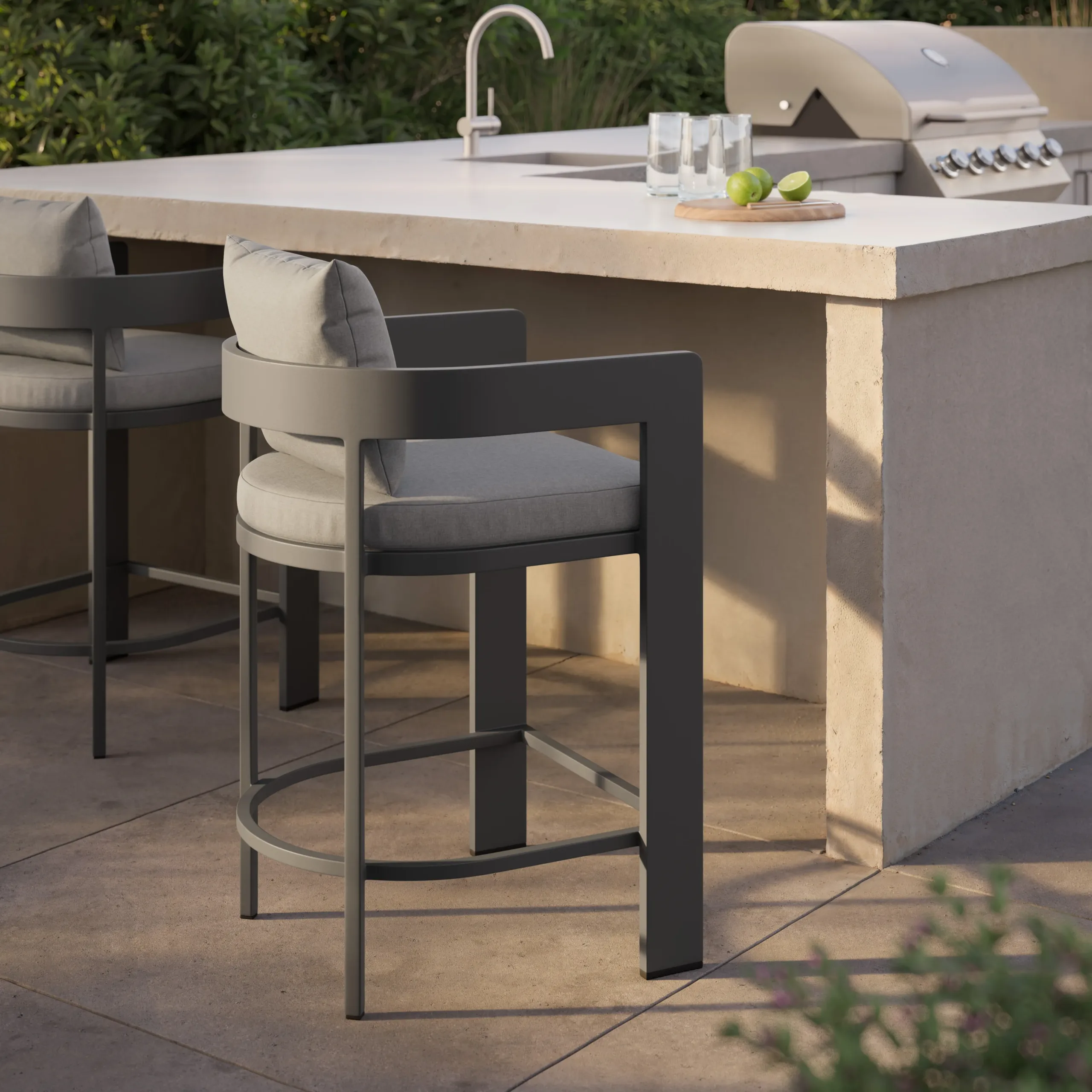 Modern gray metal outdoor barstool with round gray cushion and curved back at a concrete countertop with sink and grill.