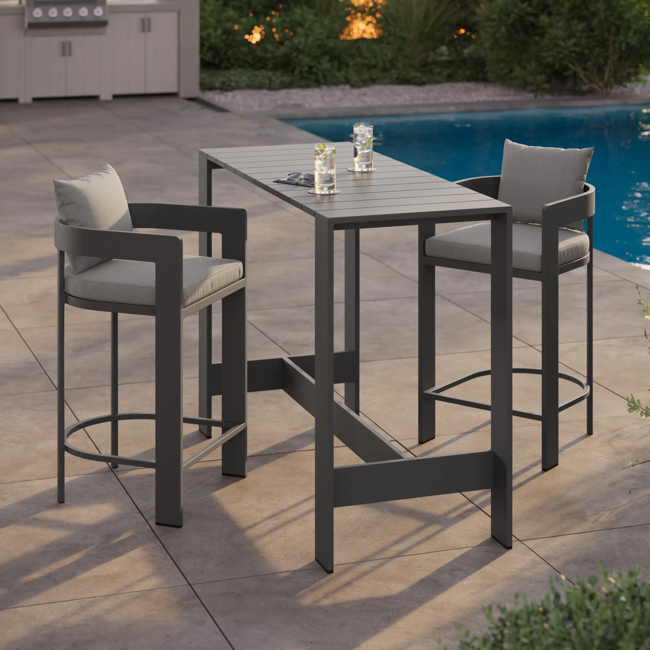 Outdoor high patio table with two gray metal bar stools with light cushions and curved armrests beside a swimming pool.