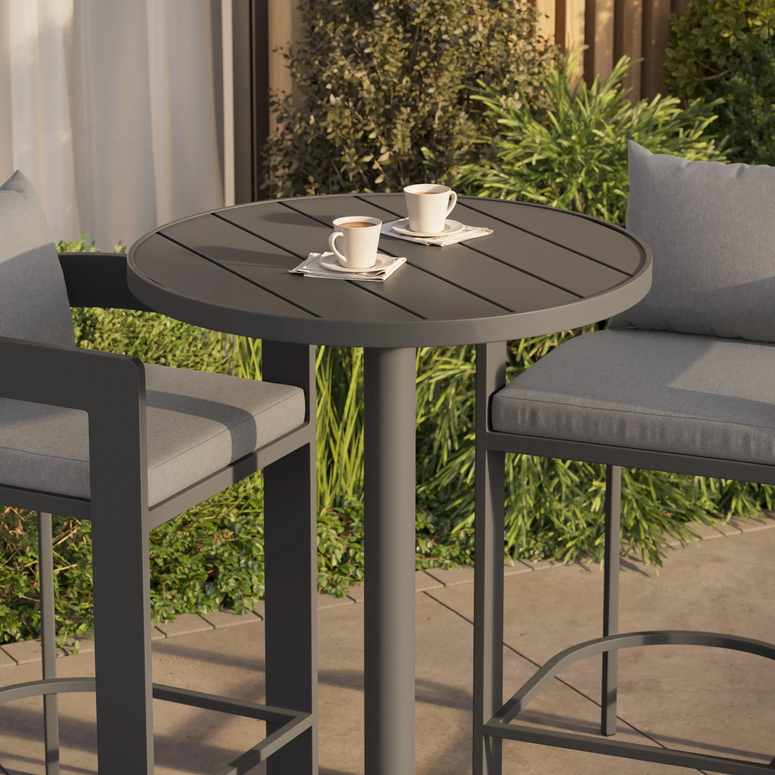 Round gray outdoor bistro table holding two coffee cups on napkins, flanked by two gray cushioned bar stools.